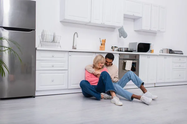 Positive Multiethnic Couple Hugging Sitting Floor Modern Kitchen — Stock Photo, Image