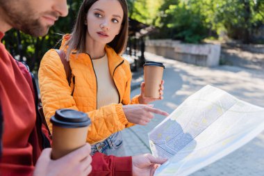 Turist elinde kahve tutup açık hava sevgilisinin yakınındaki haritayı işaret ediyor. 