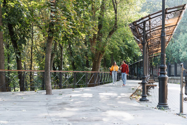 Couple of travelers with coffee to go and backpacks walking on urban street 