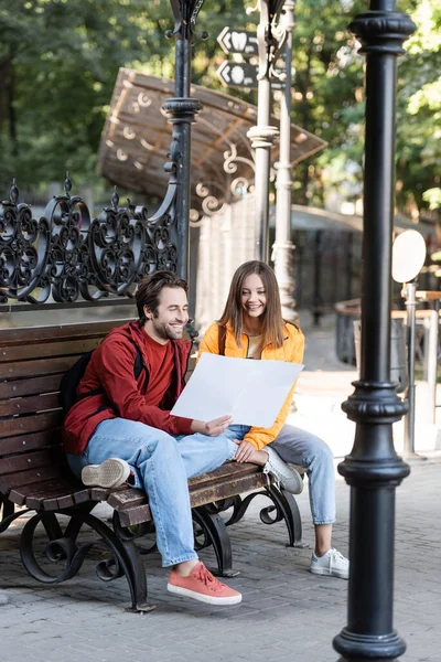 笑顔のカップル地図を見ながらベンチに座って屋外 — ストック写真