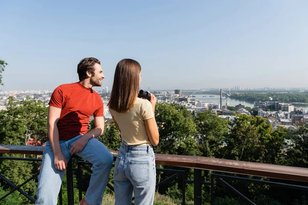 Happy traveler looking away near girlfriend with binoculars on viewpoint outdoors