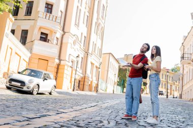 Dürbün ve harita taşıyan bir çift gezgin şehir caddesinde konuşurken 