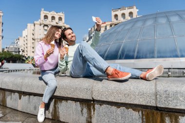 Dondurmalı turistler, şehir caddesinde akıllı telefondan selfie çekiyor. 