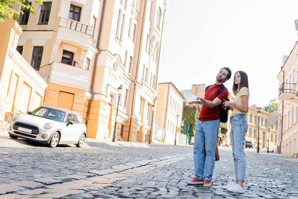 Dürbün ve harita taşıyan bir çift gezgin şehir caddesinde konuşurken 