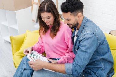 Positive multiethnic couple looking at color palette on couch at home 