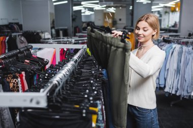 Positive young woman looking at pants in vintage shop 
