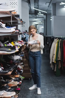 Young woman holding shoe near footwear in vintage shop 