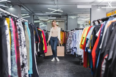 Smiling woman holding shopping bags and looking at camera in second hand