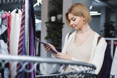 Young customer touching clothes on blurred rack in vintage market 