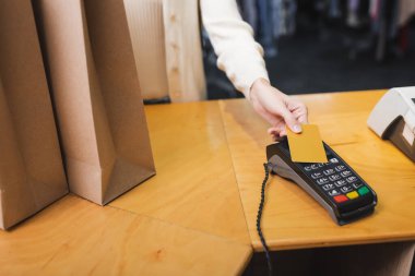 Cropped view of blurred woman paying with credit card near shopping bags in second hand 