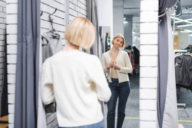 Blurred woman looking at mirror in dressing room in second hand 