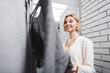 Smiling woman looking at clothes in dressing room in second hand 
