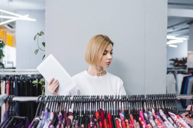 Retailer holding digital tablet near clothes on rack in vintage store 