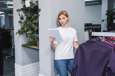İkinci el kıyafetlerin yanında dijital tablet kullanan sarışın perakendeciler. 