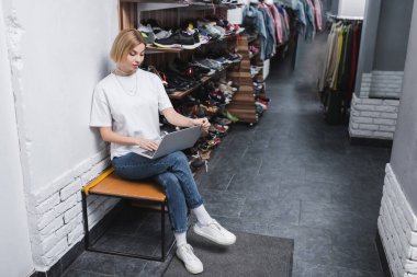 Blonde perakendecisi, vintage mağazasında ayakkabıların yanında laptop kullanıyor. 