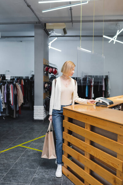 Woman holding shopping bags and paying with credit card in second hand 