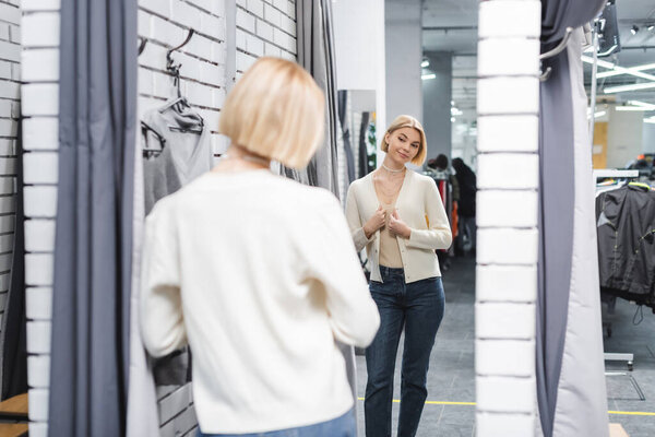 Blurred woman looking at mirror in dressing room in second hand 