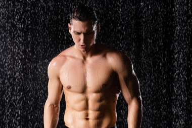 wet man with perfect body standing under falling water drops on black background clipart