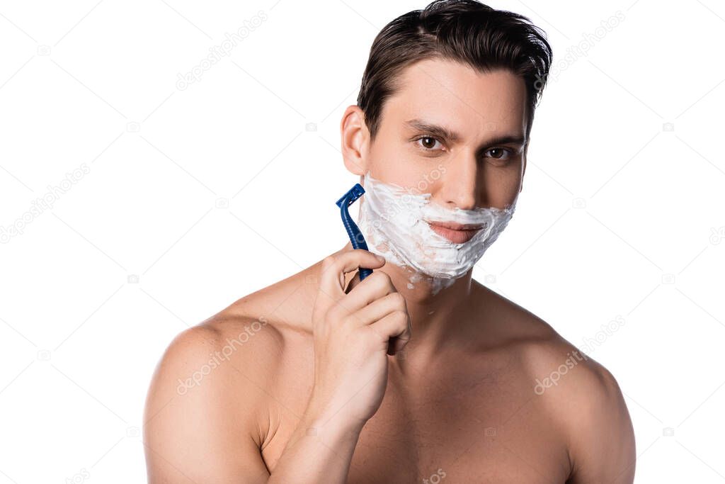 brunette man with bare shoulders looking at camera while shaving isolated on white