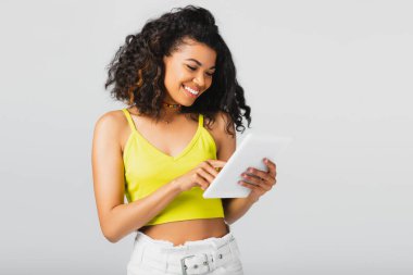 Sarı ekili bluzlu neşeli Afro-Amerikalı kadın gri tablet taşıyor.