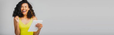 Sarı bluzlu neşeli Afro-Amerikalı kadın elinde dijital tablet tutuyordu. Gri pankartta.
