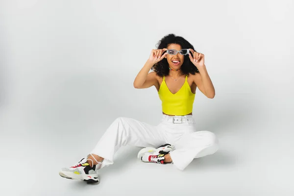 Alegre Afroamericana Mujer Ajustando Azul Gafas Sol Sobresaliendo Lengua Mientras —  Fotos de Stock