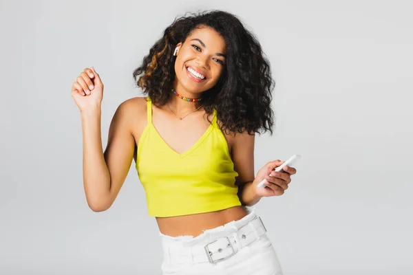 Alegre Mujer Afroamericana Auricular Inalámbrico Celebración Teléfono Inteligente Aislado Gris —  Fotos de Stock