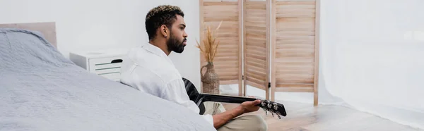 Barbudo Joven Afroamericano Hombre Tocando Guitarra Acústica Cerca Cama Bandera — Foto de Stock