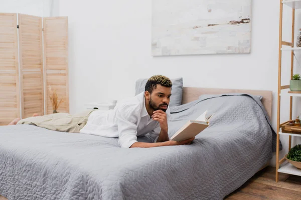 年轻的非洲裔美国男人 躺在床上 染发看书 — 图库照片