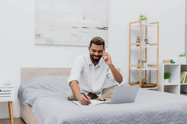 Happy African American Man Smiling While Talking Smartphone Writing Notebook — Stock Photo, Image