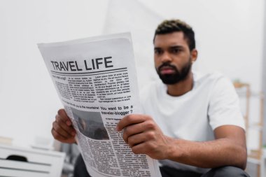 Ciddi bir Afrikalı Amerikalı sakallı adam seyahat gazetesi okuyor.