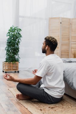 Kablosuz kulaklıklı sakallı Afrikalı Amerikalı adam evde yatarken meditasyon yapıyor.