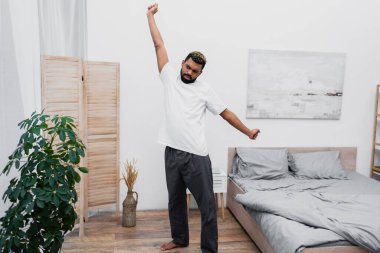 bearded african american man stretching near folding screen in modern bedroom  clipart