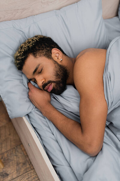 high angle view of bearded african american man with closed eyes sleeping in bed