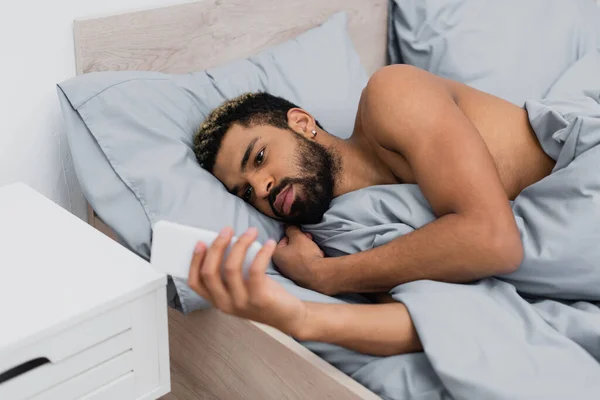 Γενειοφόρος Αφρικανός Αμερικανός Άνθρωπος Χρησιμοποιώντας Smartphone Ενώ Βρίσκεται Στο Κρεβάτι — Φωτογραφία Αρχείου