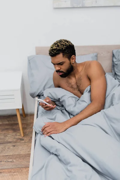 Shirtless Αφροαμερικανός Άνδρας Βαμμένα Μαλλιά Μηνυμάτων Στο Smartphone Στο Κρεβάτι — Φωτογραφία Αρχείου