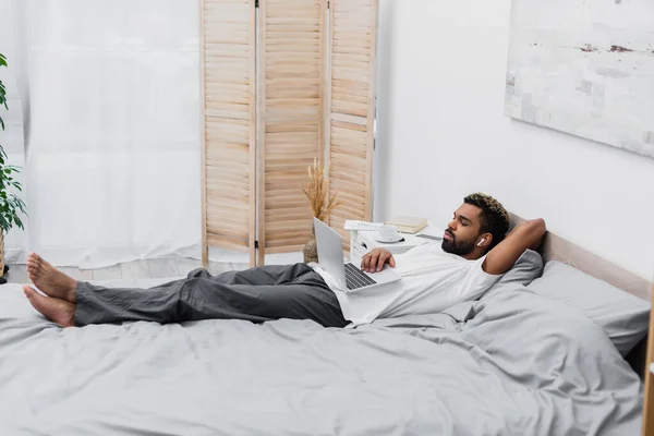 Afrikaans Amerikaanse Man Draadloze Oortelefoon Kijken Film Terwijl Liggend Bed — Stockfoto