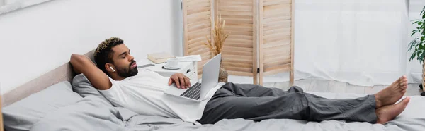 Hombre Afroamericano Auriculares Inalámbricos Viendo Película Mientras Está Acostado Cama — Foto de Stock