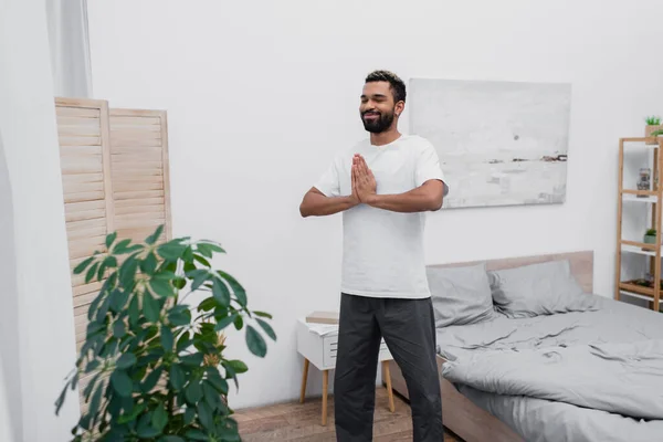 happy african american man african american man meditating with praying hands near folding screen