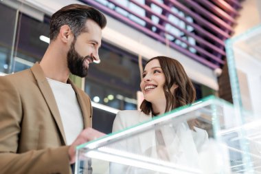 Low angle view o smiling couple looking at each other near showcase in jewelry shop 