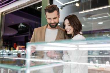 Smiling couple looking at blurred showcase in jewelry shop 