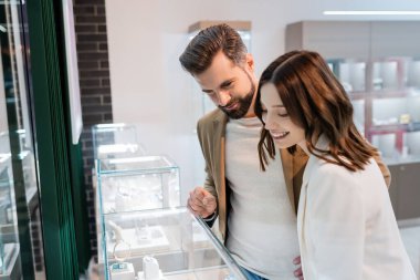 Man looking at showcase with jewelry near smiling girlfriend in store 