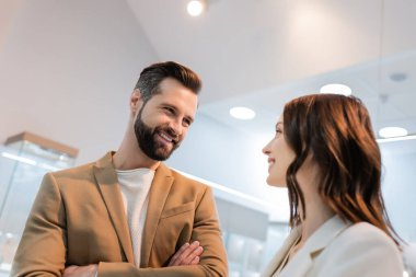 Smiling man with crossed arms looking at girlfriend in jewelry store 