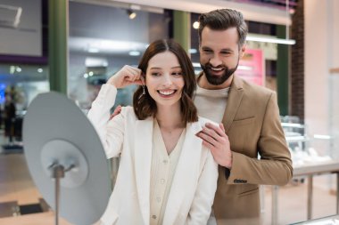 Smiling man hugging girlfriend with earring in jewelry shop 