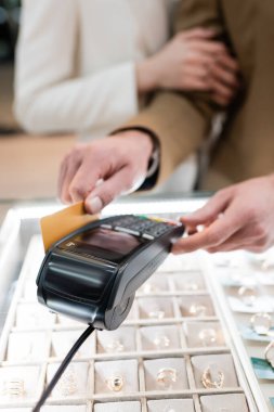 Cropped view of customer paying with credit card near blurred girlfriend in jewelry shop 