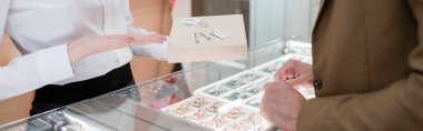 Cropped view of seller pointing at accessories near customer in jewelry shop, banner 