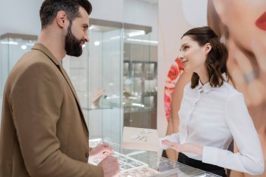 Side view of customer looking at seller pointing with hand at jewelry in shop 