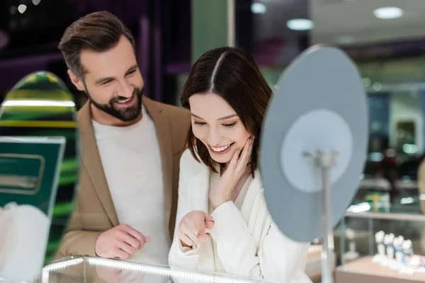 Smiling Woman Pointing Showcase Blurred Boyfriend Jewelry Shop — Stock fotografie