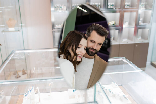 Smiling couple reflecting in mirror of jewelry shop 