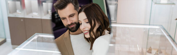 Positive couple reflecting in mirror in jewelry store, banner 